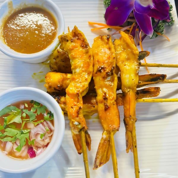 Grilled chicken satay skewers with peanut sauce and sweet chili sauce, garnished with an orchid.
