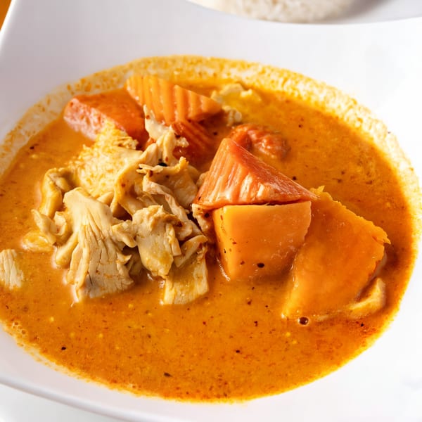Close-up of a vibrant orange Thai curry with chicken and large chunks of sweet potato.
