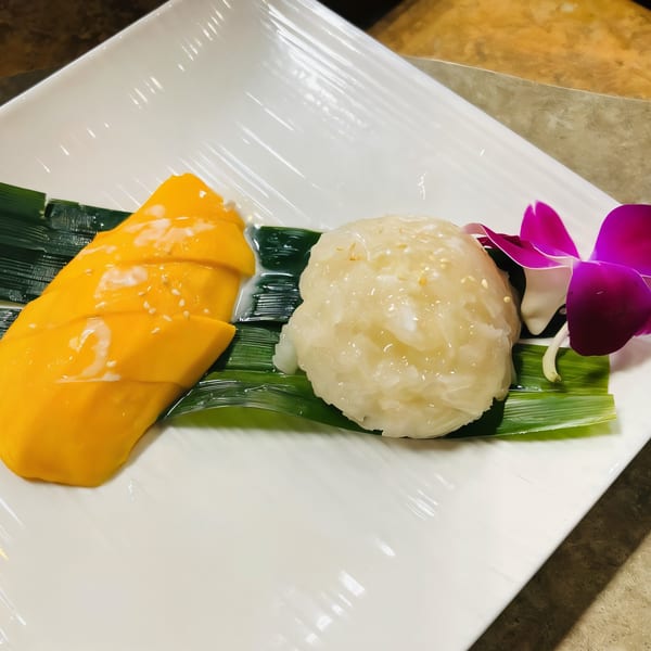 Mango sticky rice with coconut milk and sesame seeds, garnished with a purple orchid.